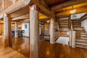 A spacious log cabin interior with a central wooden staircase, a kitchen area, and a dining space. - Log Masterpiece with 5 Master Suites, Pool Table, Hot Tub (Silverthorne)