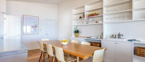 Una cocina moderna con armarios blancos, una mesa de comedor de madera y sillas. Hay un ventilador de techo, un refrigerador blanco y una planta en maceta sobre la encimera.