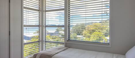 Una camera da letto con un letto, una finestra con persiane e vista su un corpo d'acqua e vegetazione.