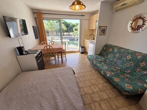 Een knus verblijf met een kitchenette, een bank, een eettafel met stoelen, en een aan de muur bevestigde televisie.