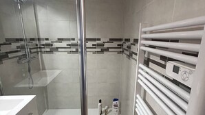 Un baño moderno con ducha envuelta en vidrio, un lavabo blanco y un perchero con panel de control.
