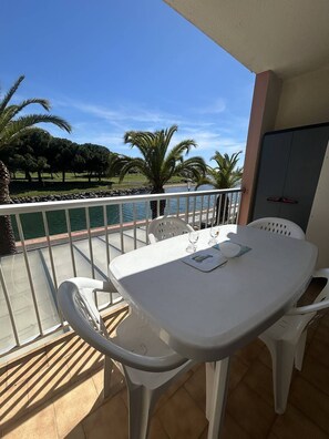 Een balkon met een tafel en stoelen, met uitzicht op een wateroppervlak en palmbomen.