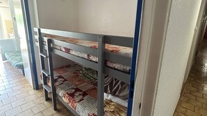 Cama literaria con varias camas, piso de baldosas y una puerta que da a otra habitación.