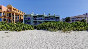 Een strandhotel met meerlaags gebouwen, een zandstrand op de voorgrond en weelderige begroeiing achterin.