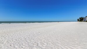 Een breed, wit zandstrand met een helderblauwe lucht en zee op de achtergrond.