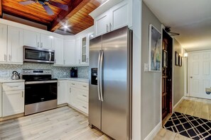 A modern kitchen with white cabinets, stainless steel appliances, and a wooden ceiling. - Sol-Mate - Serene beachfront condo steps from the Gulf (Indian Shores)