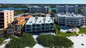 A multi-story hotel with a pool area, surrounded by greenery and a view of the water. - Sol-Mate - Serene beachfront condo steps from the Gulf (Indian Shores)