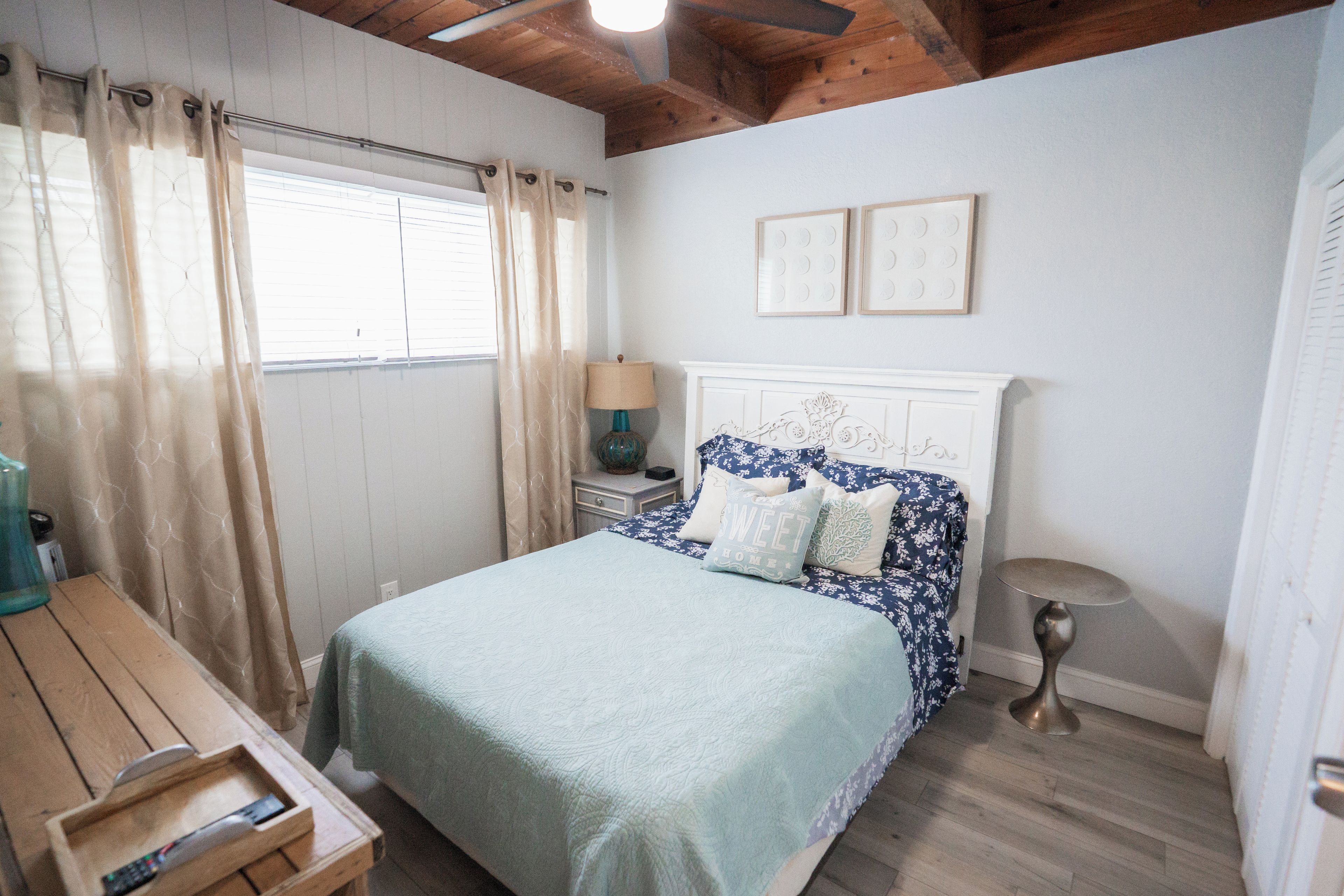 A bedroom with a bed, a nightstand, a lamp, a window with curtains, and a door.