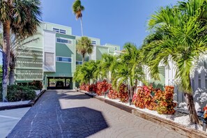 A hotel entrance with a paved walkway, palm trees, and a building with a green facade. - Sol-Mate - Serene beachfront condo steps from the Gulf (Indian Shores)