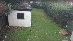Un petit bâtiment blanc, de plain-pied, doté d’une fenêtre, entouré d’une pelouse bien entretenue et d’une végétation dense.