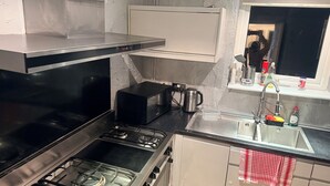 Une cuisine compacte équipée d’une cuisinière à gaz, d’un four à micro-ondes, d’une bouilloire et d’un évier avec un robinet.