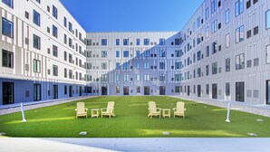 A modern building with a courtyard featuring artificial grass, outdoor seating, and a clear sky. - Across from Clinic | 2 Bed/2 Bath | Free Garage (Cleveland)