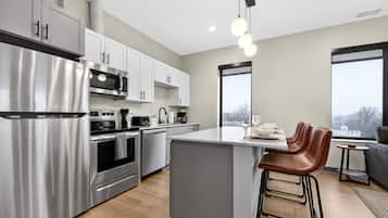A modern kitchen with stainless steel appliances, a central island, and a seating area with stools.