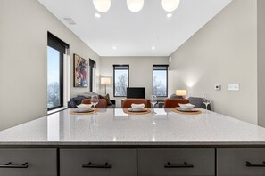 Una cocina moderna con una isla grande, dos sofás, un televisor y una zona de comedor con una mesa preparada para dos.