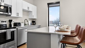 A modern kitchen with white cabinets, stainless steel appliances, and a large island with bar stools. - Across from Clinic | 2 Bed/2 Bath | Free Garage (Cleveland)