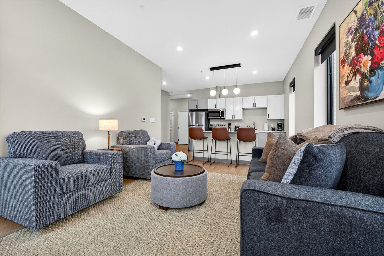 A modern living room with grey sofas, a round coffee table, and a kitchen in the background.