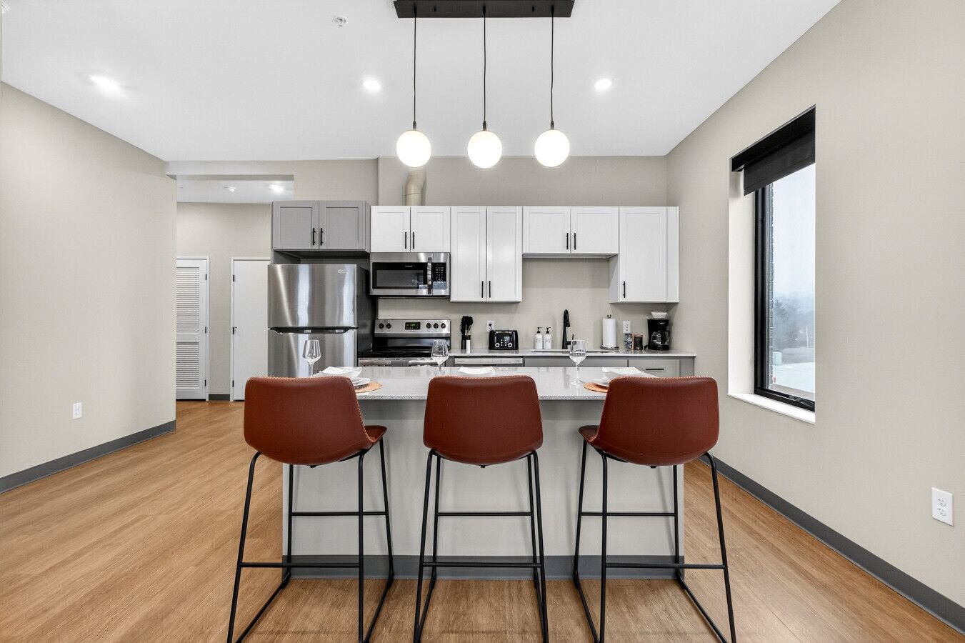 A modern kitchen with white cabinets, stainless steel appliances, and a bar area with three stools.