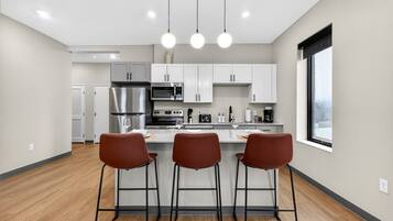 A modern kitchen with white cabinets, stainless steel appliances, and a bar area with three stools.