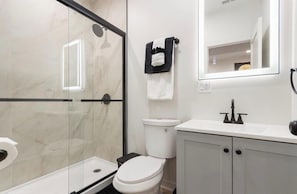 Een moderne badkamer met een douchecabine van glas, een toilet en een wastafel met spiegel erboven.