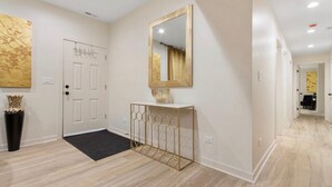 A hallway with a white door, a console table with a gold frame, and a large mirror on the wall.