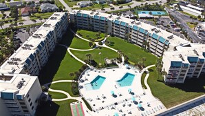 Ein mehrstöckiges Hotel mit Innenhof, der zwei Schwimmbecken, üppiges Grün und Palmen umfasst.