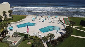 Ein Resort mit zwei Schwimmbecken, einer Flagge und einem Strandbereich mit Sonnenschirmen und Liegestühlen.