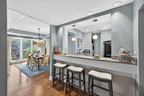 A modern kitchen with a large island, bar stools, and a dining area with a wooden table and chairs. - Discover Kiawah at 4922 Turtle Point, a stunning 3-bedroom with golf views! (Kiawah Island)