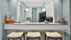Une cuisine dotée d’un îlot central, de luminaires suspendus et donnant sur la salle à manger adjacente.