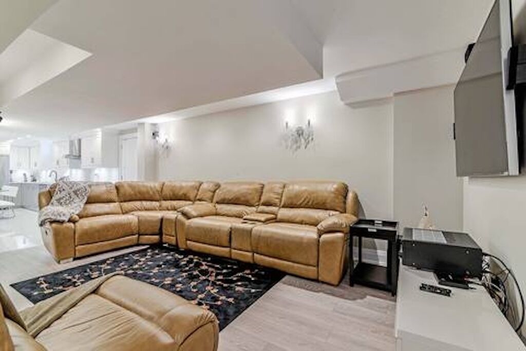 A modern living room with a large L-shaped sectional sofa, a small side table, and a flat-screen TV mounted on the wall.