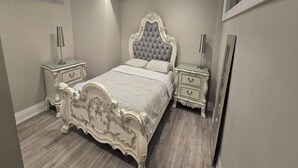 Quarto com cama de cabeceira estofada, duas mesas de cabeceira com luminárias e um espelho grande na parede.