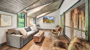 Uma sala de estar estilo loft, com teto de madeira, um sofá, uma poltrona e um quadro na parede.