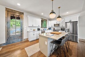 A modern kitchen with white cabinets, stainless steel appliances, and a central island with bar stools. - Black Diamond at Eagles Nest: Views, Hot Tub, Pet Friendly! (Banner Elk)