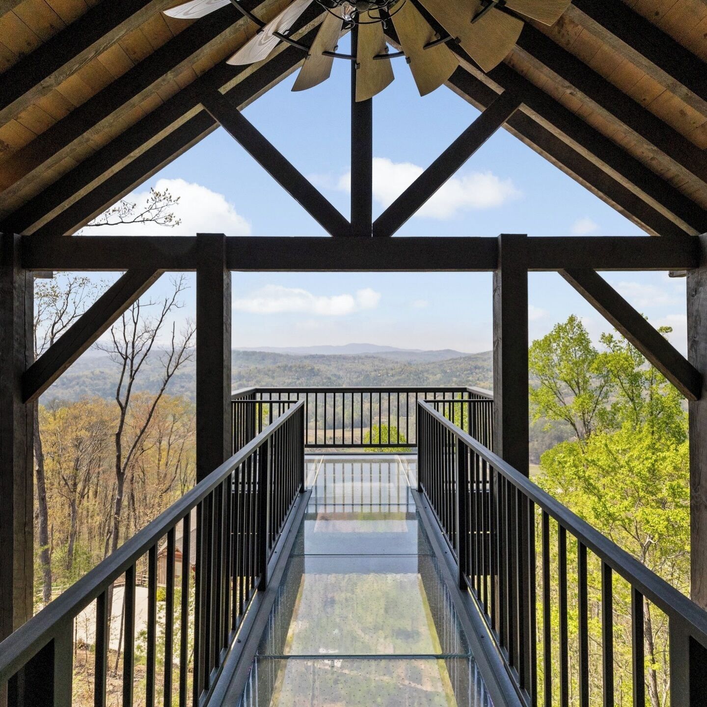 A wooden structure with a glass floor leading to a balcony with a mountain view.