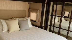 Uma cama grande com um edredom branco acolchoado, uma cabeceira de madeira e uma janela com vista.