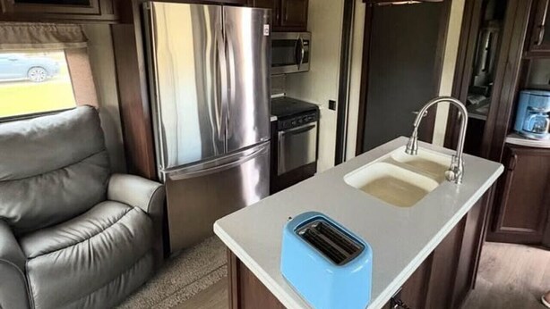Cozinha compacta de motorhome, equipada com geladeira, micro-ondas e pia.