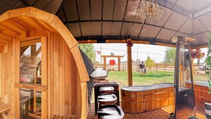 Eine Holzhütte mit überdachter Terrasse, einer Sauna und einem Whirlpool.