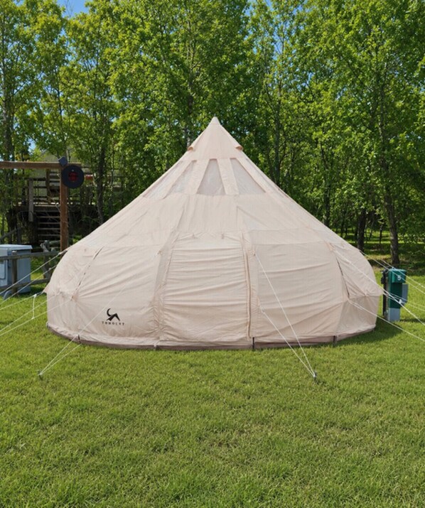 A large, dome-shaped tent with a peaked roof, set up on a grassy field with trees in the background.