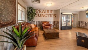 Eine Lobby mit braunem Ledersofa, einem Holztisch, einem Ledersessel und einer großen Pflanze. An der Wand befindet sich ein Schild mit der Aufschrift "Prairie Junction".