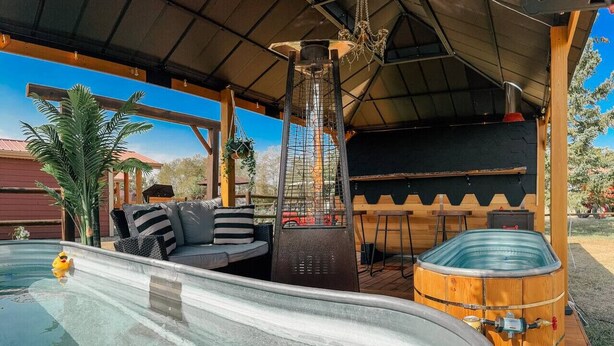 Ein Bereich mit Whirlpool, einer Holzterrasse, einer Lounge mit Kissen und einem großen Warmwasserbereiter.