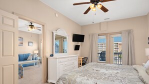 Een slaapkamer met een groot bed, een dressoir, een televisie en een balkon met uitzicht op de stad.