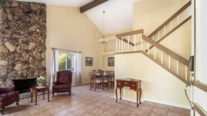A spacious living room with a stone fireplace, a dining area, and a wooden staircase. - Marvelous 3-bedroom house with AC in sunny Oceanside (Oceanside)