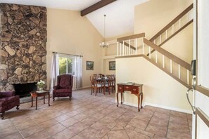 A spacious living room with a stone fireplace, a dining area, and a wooden staircase. - Marvelous 3-bedroom house with AC in sunny Oceanside (Oceanside)