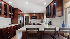 A modern kitchen with dark wooden cabinets, a large island with bar stools, and stainless steel appliances. - Marvelous 3-bedroom house with AC in sunny Oceanside (Oceanside)