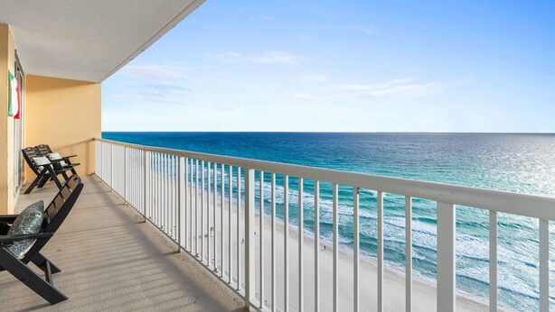 Varanda com vista para o mar, guarda-corpo branco e mesa com cadeiras.