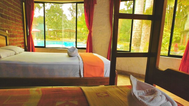 A hotel room with two beds, a wooden table, and a view of a swimming pool. - Puerto Quito Lodge - Mon Par (Puerto Quito)