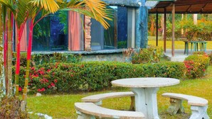 A rustic building with a blue exterior, surrounded by lush greenery and a small outdoor seating area with benches. - Puerto Quito Lodge - Mon Par (Puerto Quito)