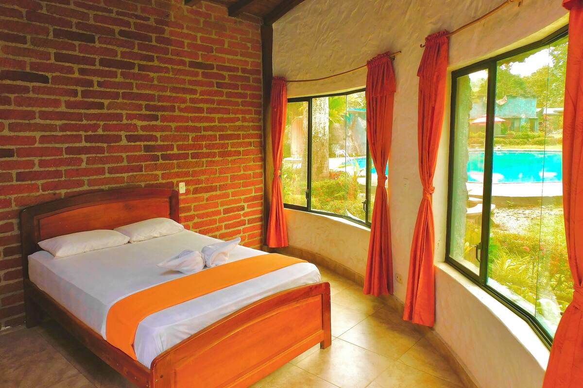 A room with a brick wall, a wooden bed, and a window with curtains.