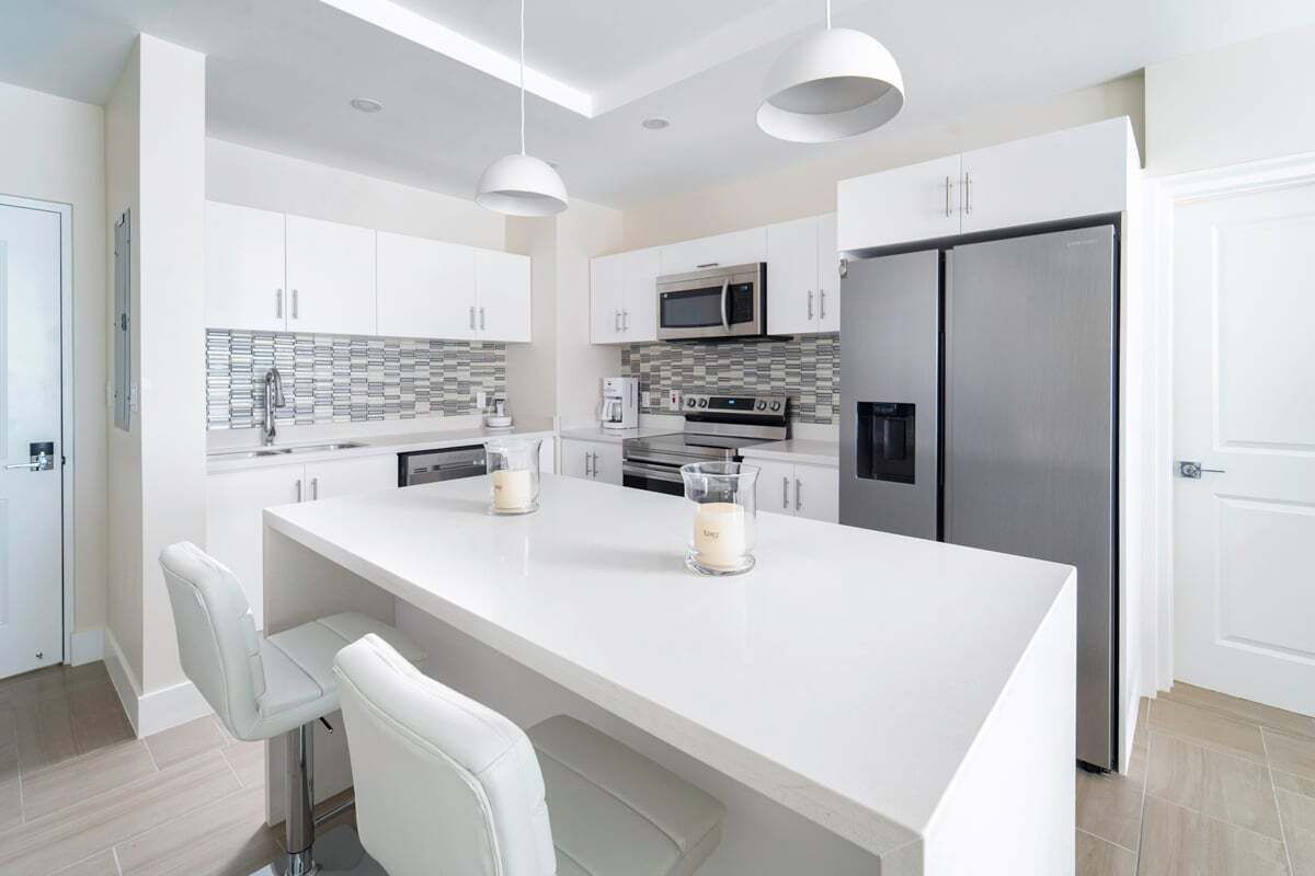 A modern kitchen with white cabinets, a large island, stainless steel appliances, and pendant lighting.