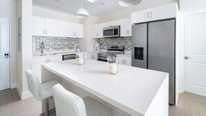 A modern kitchen with white cabinets, a large island, stainless steel appliances, and pendant lighting. - Romantic Island Retreat | Resort Pool & Sunset Rooftop (Battaleys)