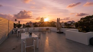 A rooftop terrace with a table set for dining, chairs, and a sun lounger. - Romantic Island Retreat | Resort Pool & Sunset Rooftop (Battaleys)
